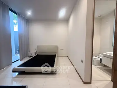 Modern bedroom with sleek design and attached bathroom, featuring minimalist decor and large windows.
