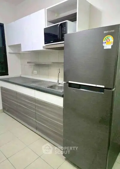 Modern kitchen with sleek cabinetry and stainless steel fridge in a compact layout.