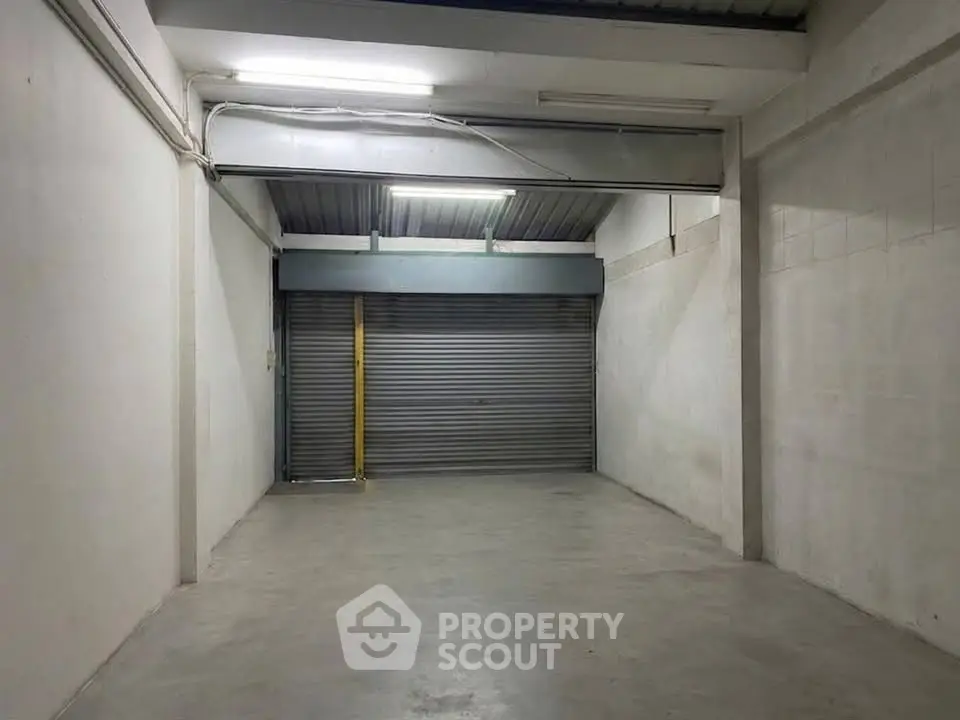 Spacious industrial garage with high ceiling and roller shutter door, ideal for storage or workshop use.