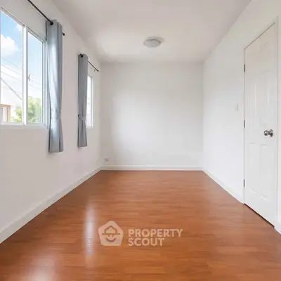 Spacious empty room with wooden flooring and natural light from windows.