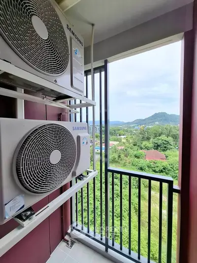 Scenic balcony view with air conditioning units overlooking lush greenery and distant hills.
