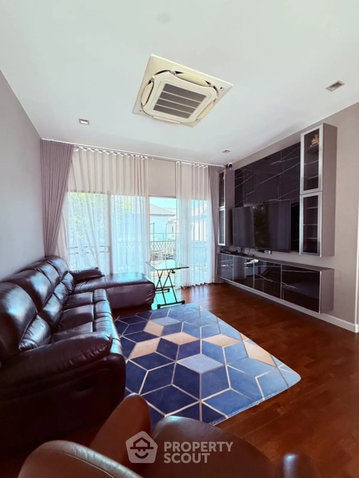 Modern living room with leather sofas and large TV unit, featuring stylish geometric rug and natural light.