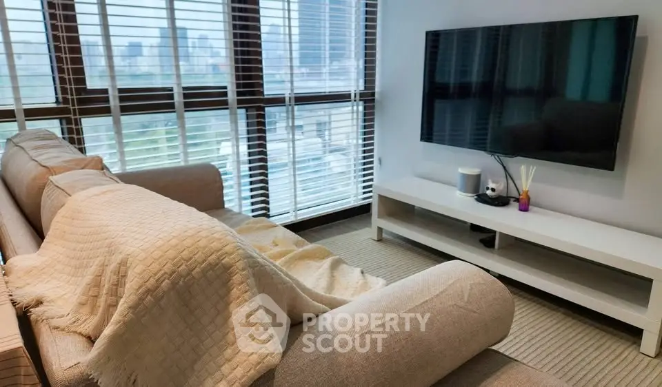 Modern living room with large windows and city view, featuring a cozy sofa and flat-screen TV.