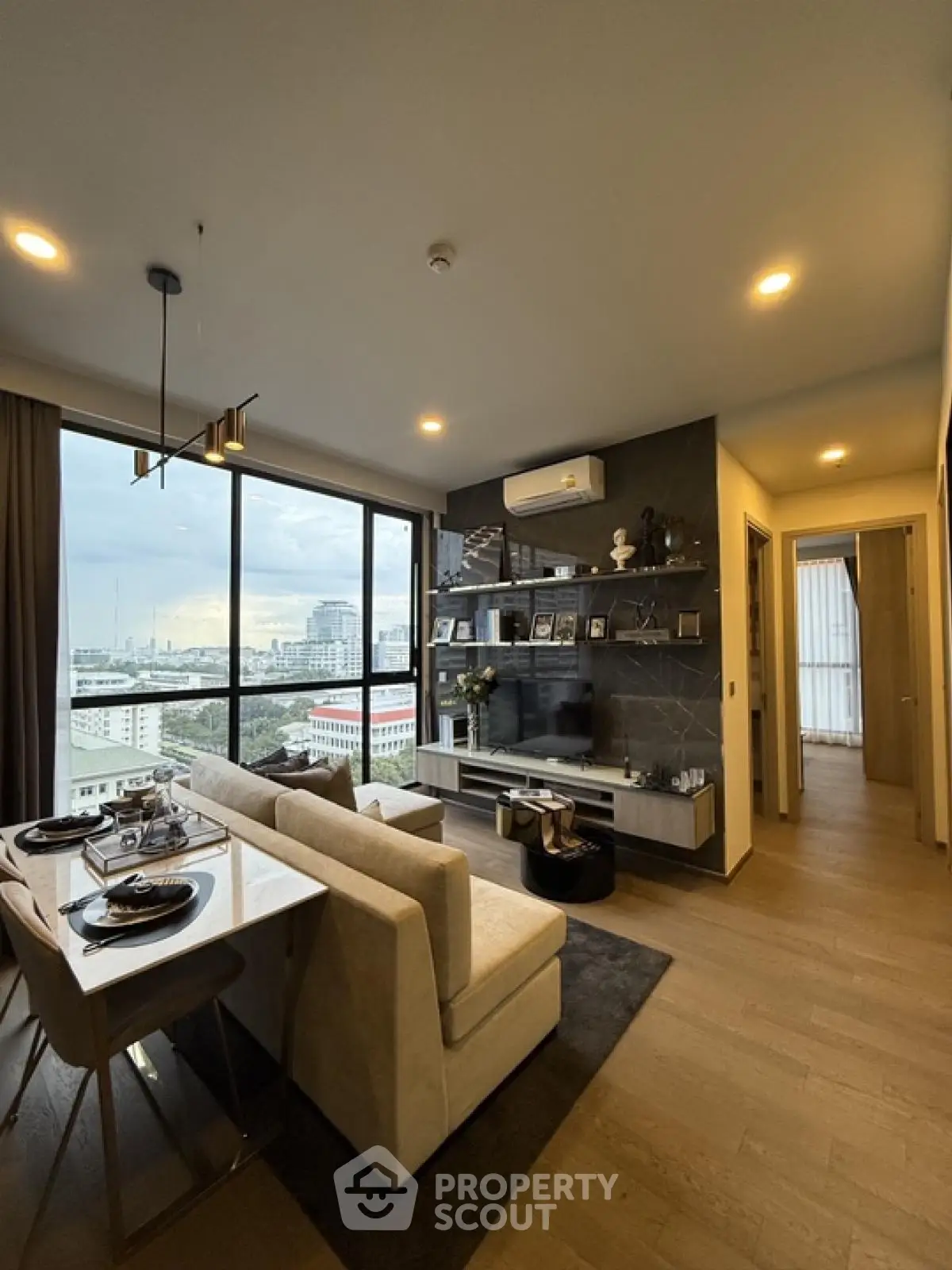Modern living room with city view, stylish decor, and open dining area in high-rise apartment.