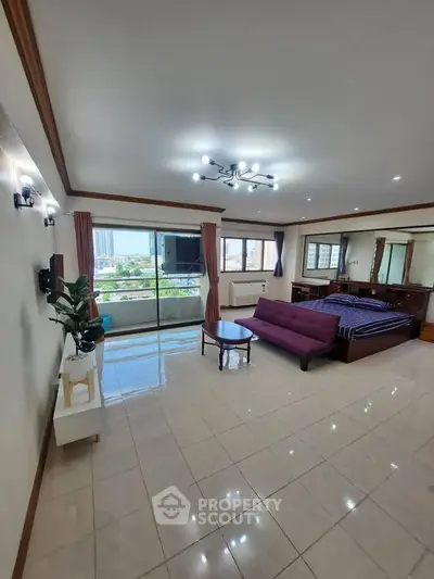 Spacious studio apartment with modern lighting and city view, featuring a cozy living area and large windows.