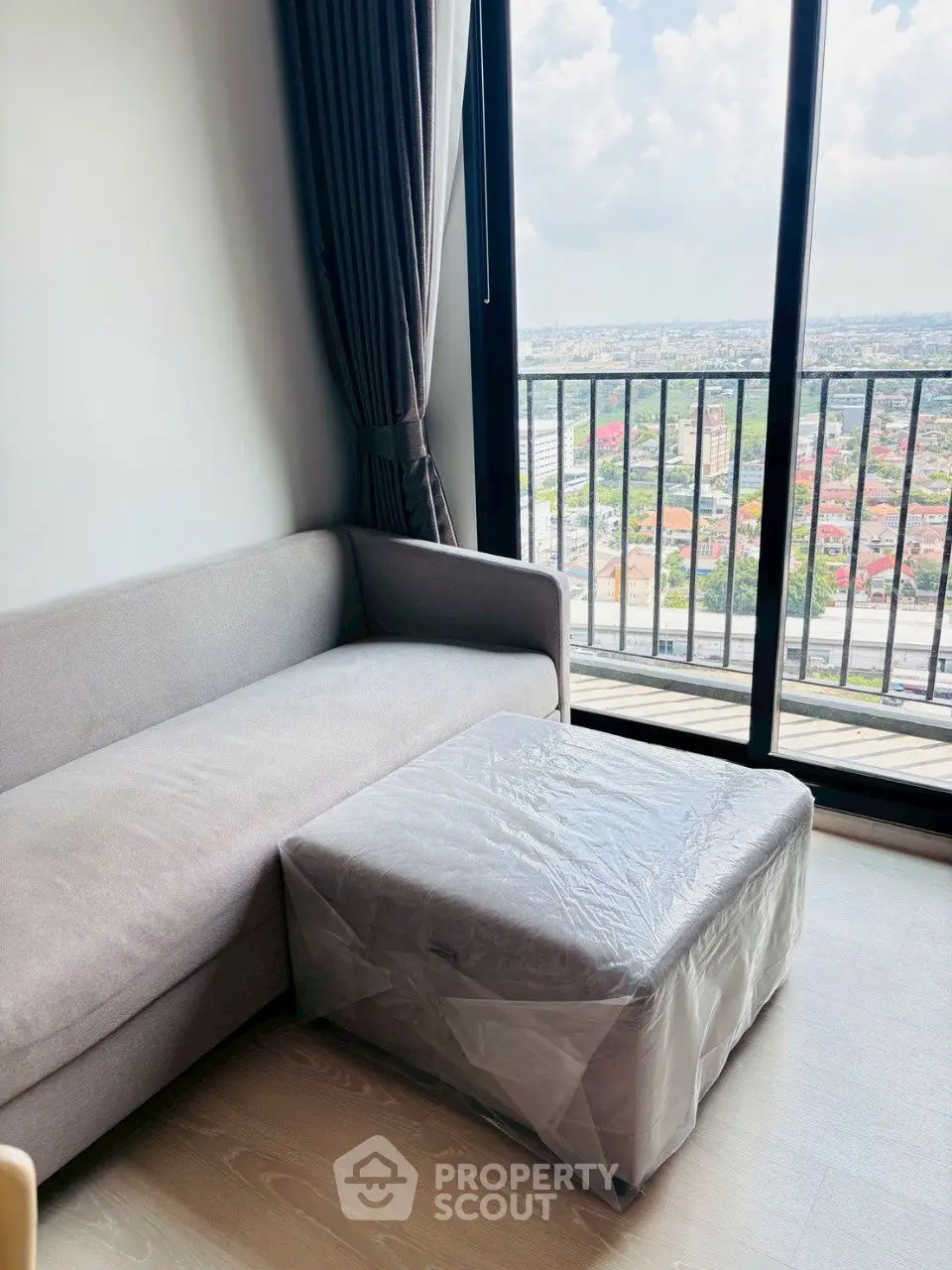 Modern living room with a stunning city view from the balcony, featuring a cozy sofa and ottoman.