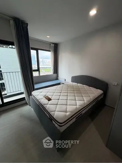 Modern bedroom with large window and city view, featuring a comfortable bed and stylish decor.