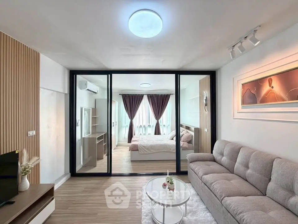 Modern living room with glass partition leading to a cozy bedroom, featuring stylish decor and natural light.