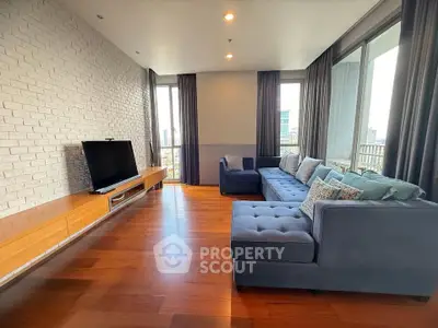 Spacious modern living room with hardwood floors and large windows offering city views.