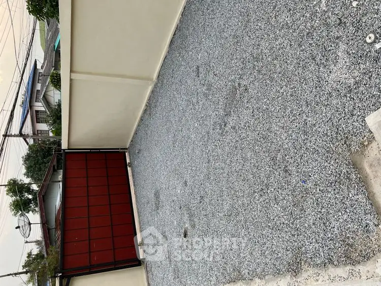 Spacious gravel driveway with secure red gate in residential area