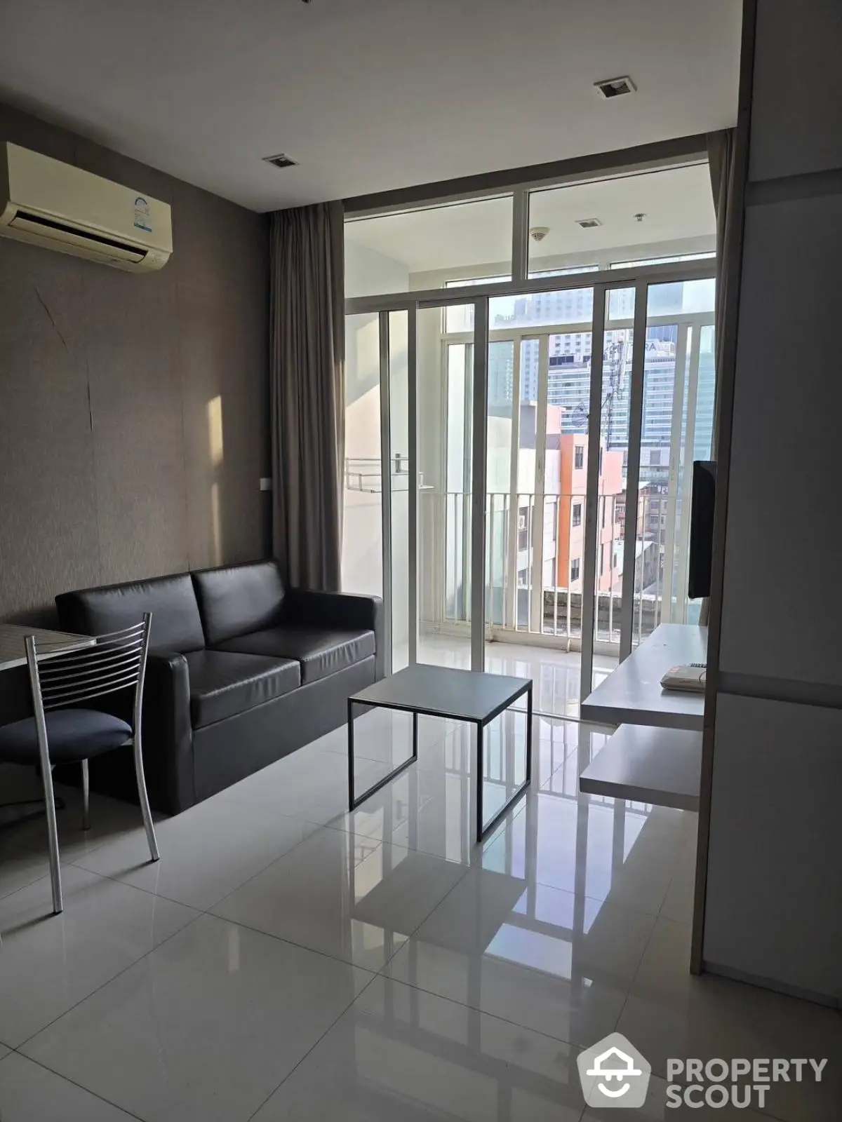 Modern living room with balcony and city view, featuring sleek furniture and air conditioning.