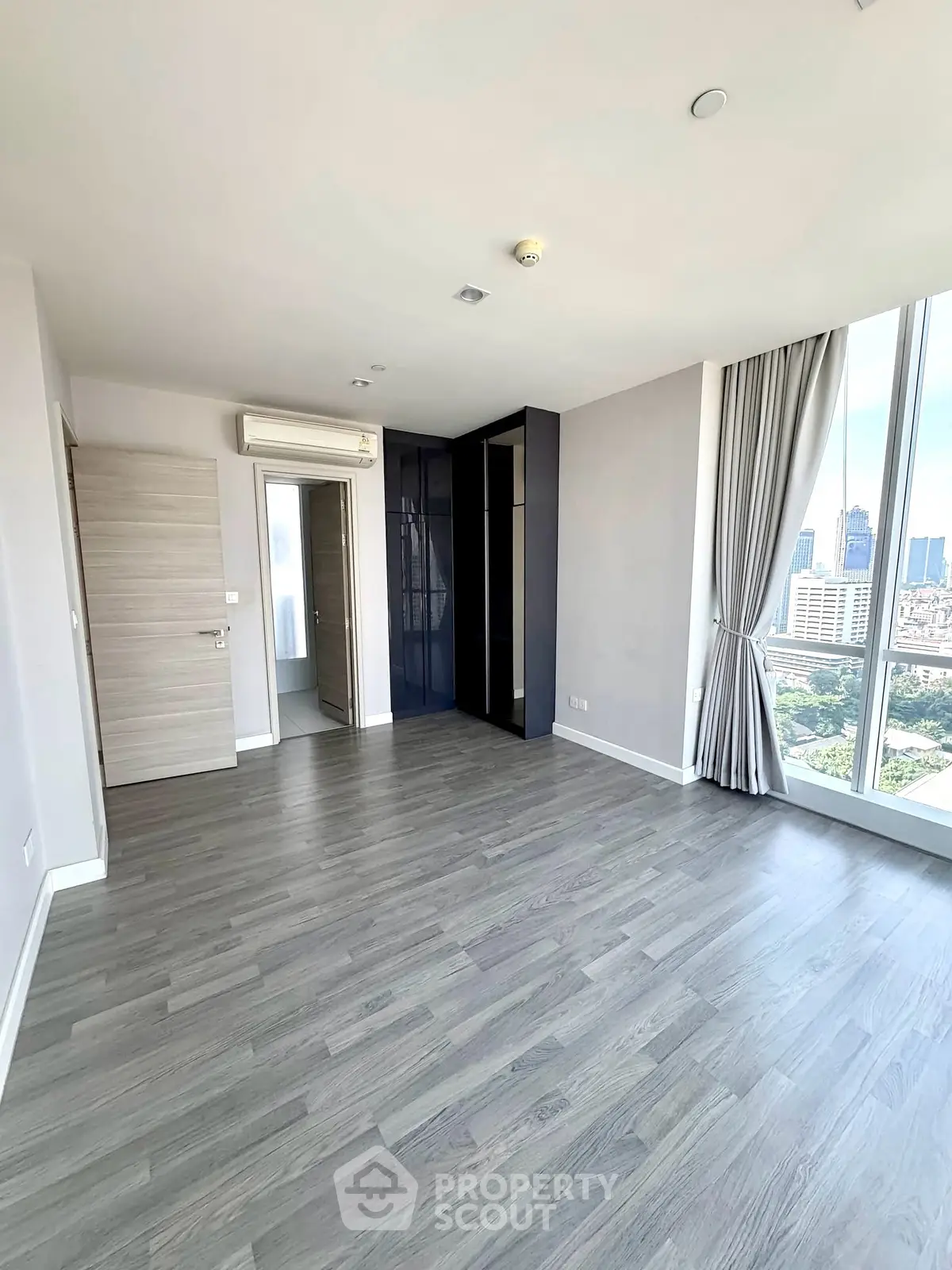 Spacious modern apartment with large windows and city view, featuring sleek flooring and neutral tones.