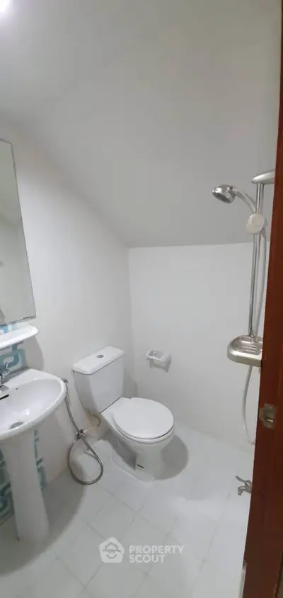 Compact bathroom with shower, toilet, and sink in a minimalist design.