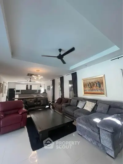 Spacious living room with modern furniture and ceiling fan, open layout to kitchen area.