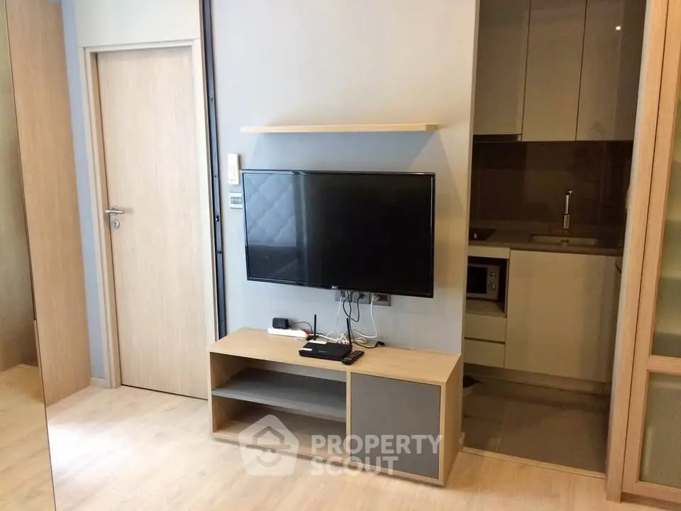 Modern living room with sleek TV setup and compact kitchen area.