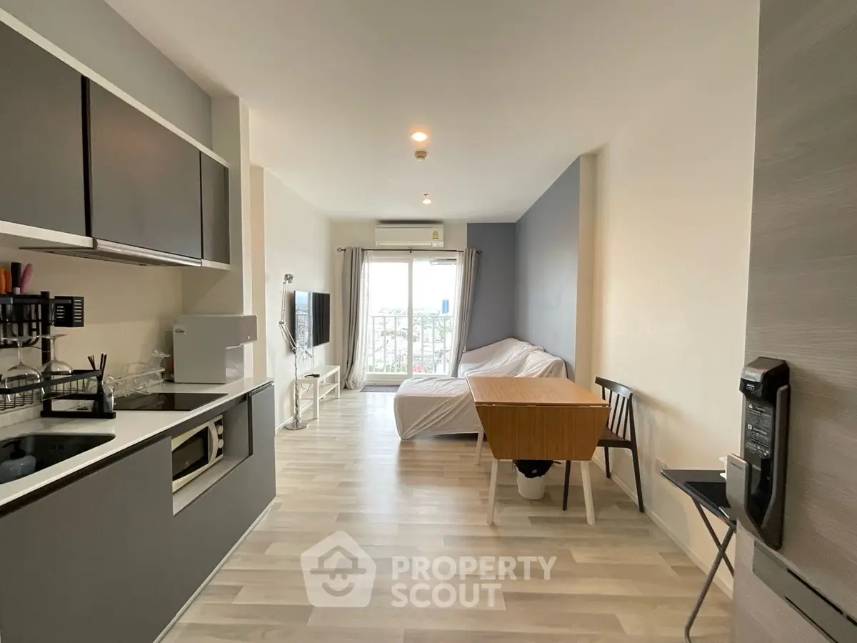 Modern open-plan studio apartment with sleek kitchen and cozy living area, featuring a large window with city views.