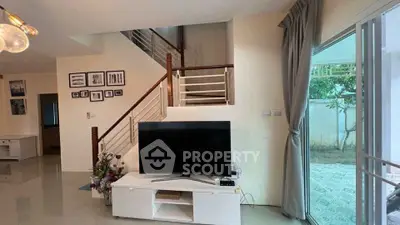 Spacious living room with modern decor and large TV, featuring a staircase and garden view.