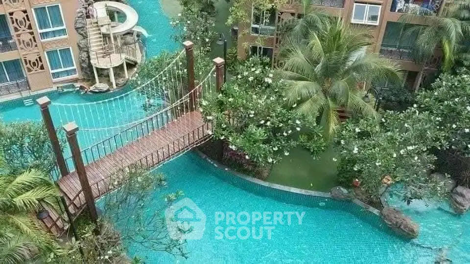 Luxurious resort-style pool with lush greenery and bridge in tropical setting.