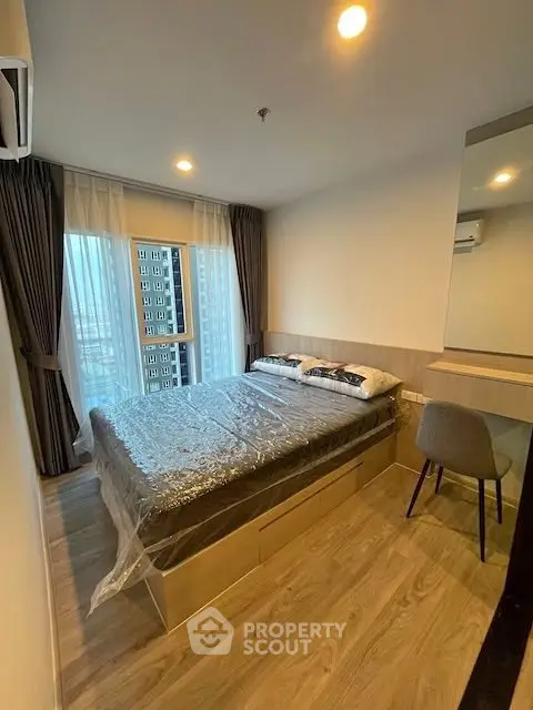 Modern bedroom with large window and wooden flooring in high-rise apartment.