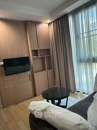 Modern living room with wooden paneling and large window, featuring a cozy sofa and sleek TV setup.