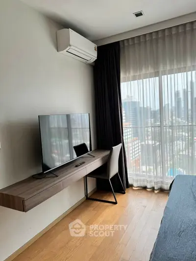 Modern bedroom with city view, featuring sleek desk, chair, and wall-mounted TV under air conditioning unit.