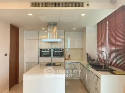 Modern kitchen with marble countertops and sleek cabinetry, featuring built-in ovens and large windows.