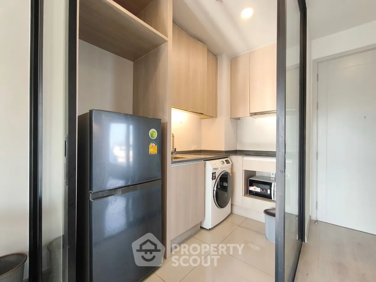 Modern compact kitchen with washing machine and fridge in sleek apartment.