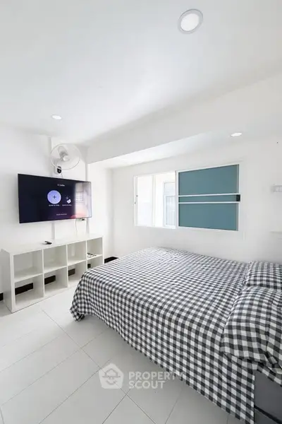 Modern bedroom with checkered bedding, wall-mounted TV, and ample natural light.