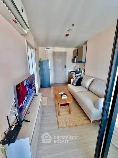 Modern living room with cozy sofa, flat-screen TV, and compact kitchen in open layout apartment.