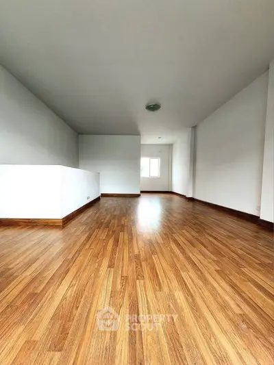 Spacious empty room with wooden flooring and bright natural light, perfect for customization.