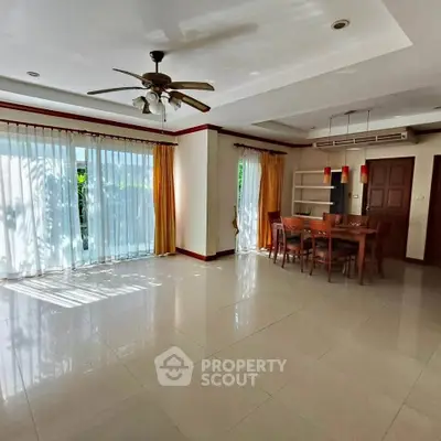 Spacious living room with dining area, large windows, and ceiling fan in modern home.