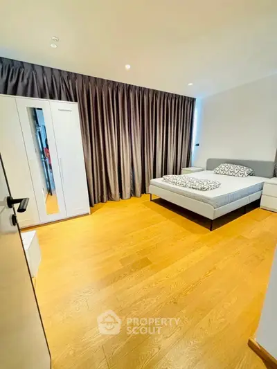 Spacious modern bedroom with wooden flooring and elegant curtains