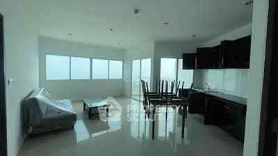 Spacious open-layout living room with modern kitchen and large windows offering natural light.