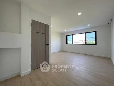 Spacious empty room with large window and wooden flooring, perfect for customization.