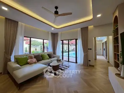 Spacious living room with modern decor and pool view, featuring large windows and elegant lighting.