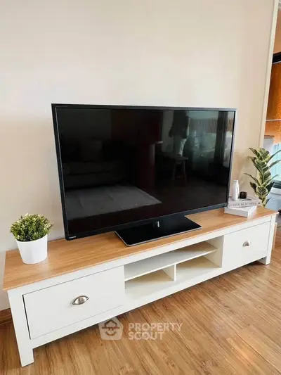 Modern living room with sleek TV stand and flat-screen TV, wooden flooring, and stylish decor.