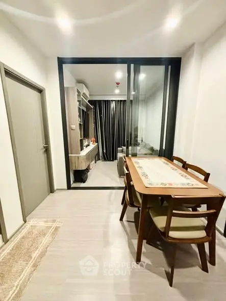 Modern dining area with wooden table and chairs, adjacent to a cozy living space with glass partition.