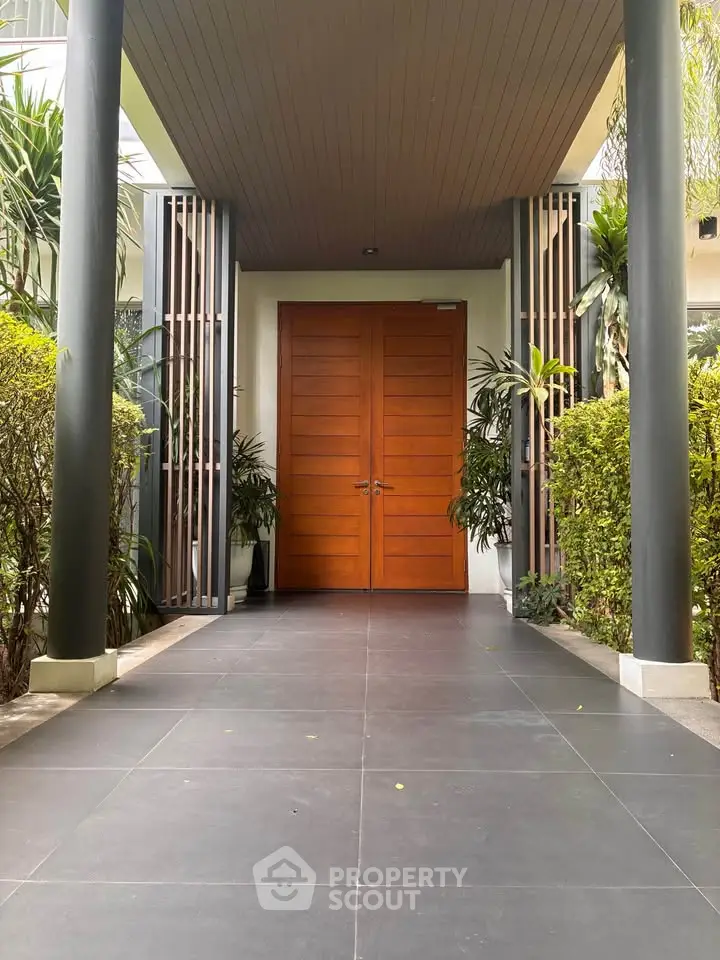 Elegant entrance with wooden double doors and lush greenery, showcasing modern architectural design.