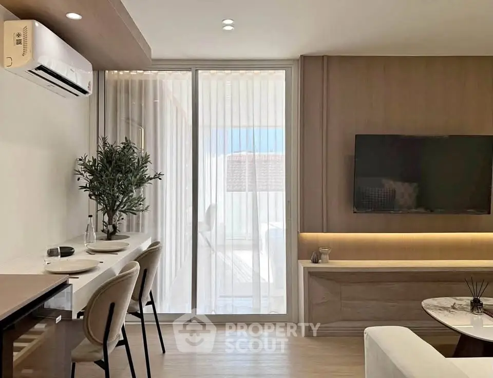 Modern living room with sleek design, featuring a wall-mounted TV, stylish furniture, and a large window with sheer curtains.