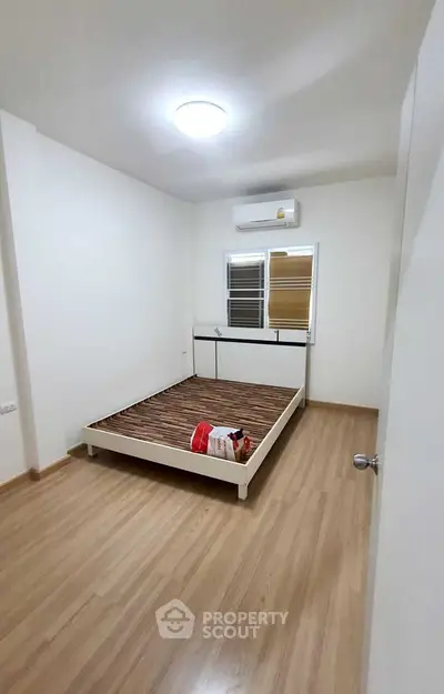 Minimalist bedroom with wooden flooring and air conditioning unit.