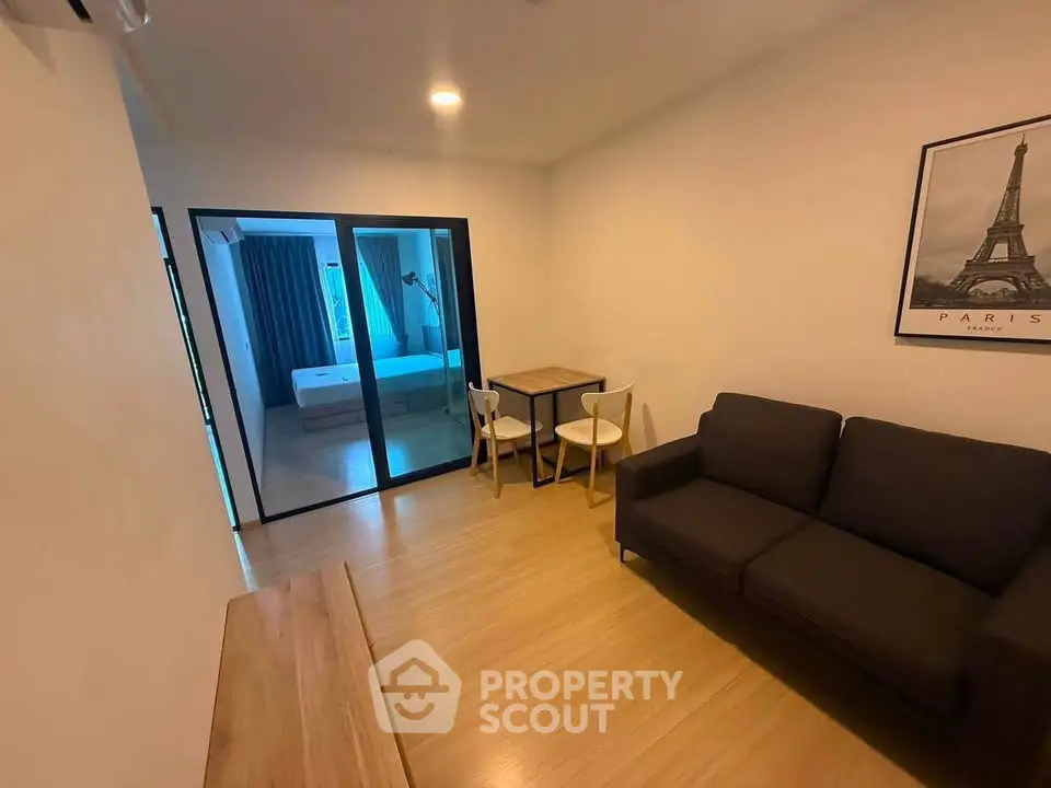 Modern living room with wooden flooring and a view into a cozy bedroom, featuring a stylish sofa and dining area.