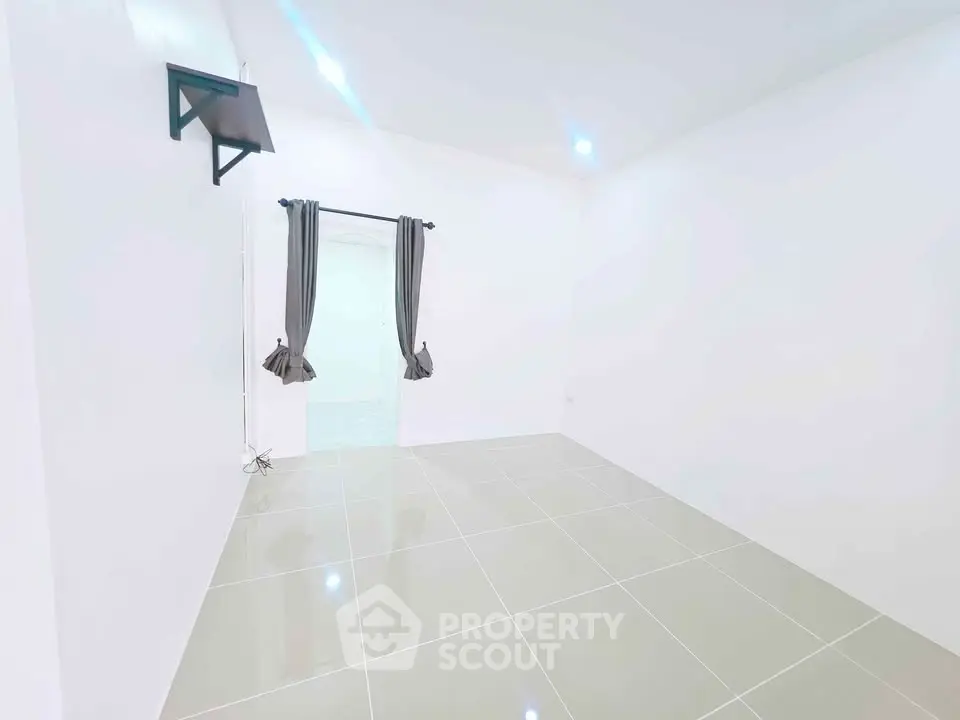 Spacious empty room with tiled floor and wall-mounted TV bracket, ideal for customization.