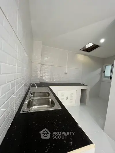 Modern kitchen with sleek black countertops and dual stainless steel sinks in a bright, tiled space.