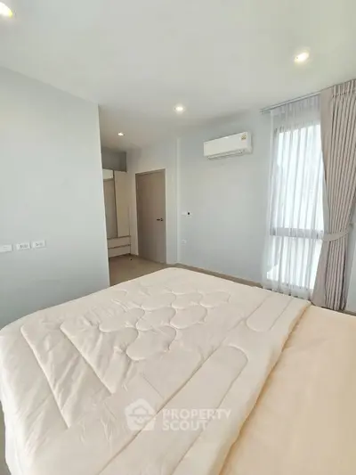 Spacious bedroom with modern decor and natural light, featuring a cozy bed and air conditioning.
