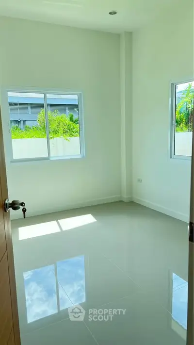 Bright empty room with glossy tile flooring and two windows overlooking greenery.