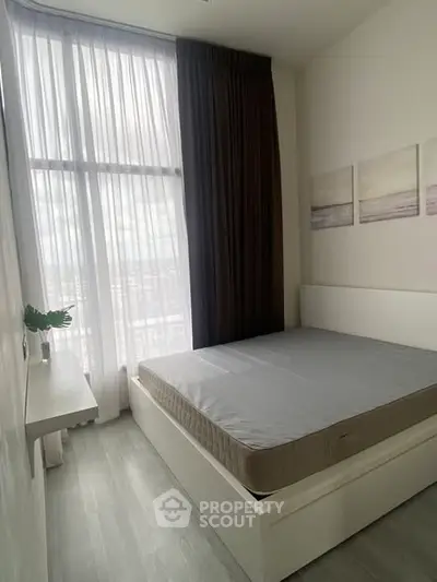Modern bedroom with high ceiling and large window, featuring minimalist decor and natural light.
