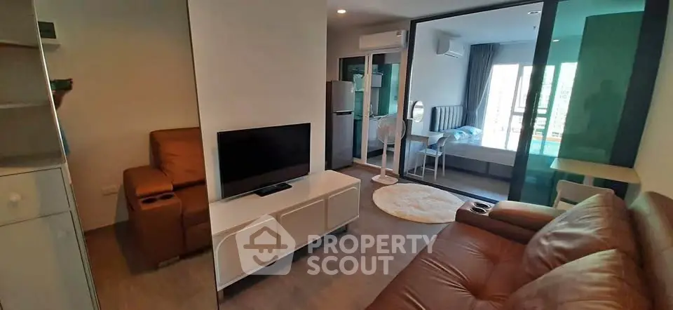 Modern living room with leather sofas and TV, adjacent to a bedroom with glass partition.