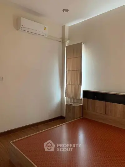 Minimalist bedroom with wooden flooring and air conditioning, featuring a built-in bed frame and natural light.