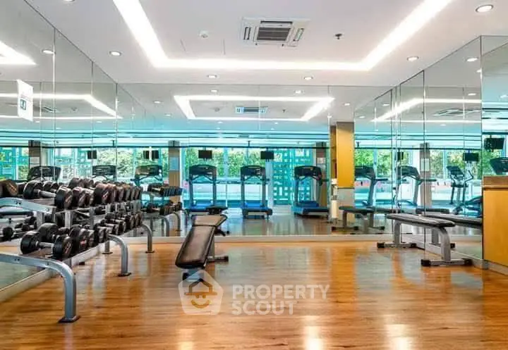 Spacious modern gym with mirrored walls and fitness equipment in luxury building.