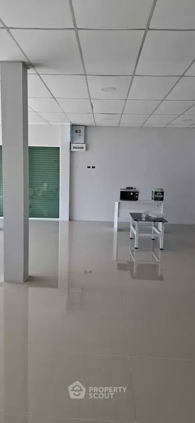 Spacious commercial space with tiled flooring and minimal furnishings, ideal for retail or office setup.